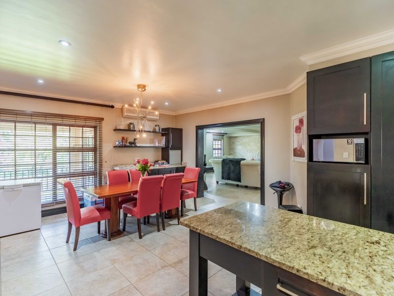 Open-plan kitchen and dining area featuring granite countertops, dark cabinetry, tiled flooring, and recessed lighting, with a seamless flow into the adjacent living space.