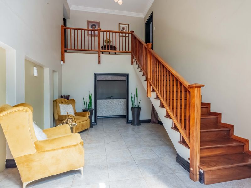 Spacious entrance hall featuring a prominent wooden staircase with balustrade and neutral tiled flooring, creating a welcoming and open transition area.