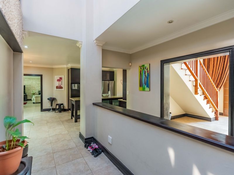 A spacious hallway featuring tiled flooring, recessed lighting, and a wooden staircase with a matching balustrade, providing an open flow between living areas.
