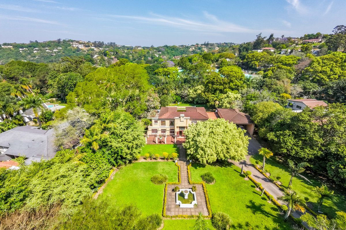 Aerial view of a large residential property featuring a spacious landscaped garden, central water feature, paved driveway, and a substantial multi-level home.