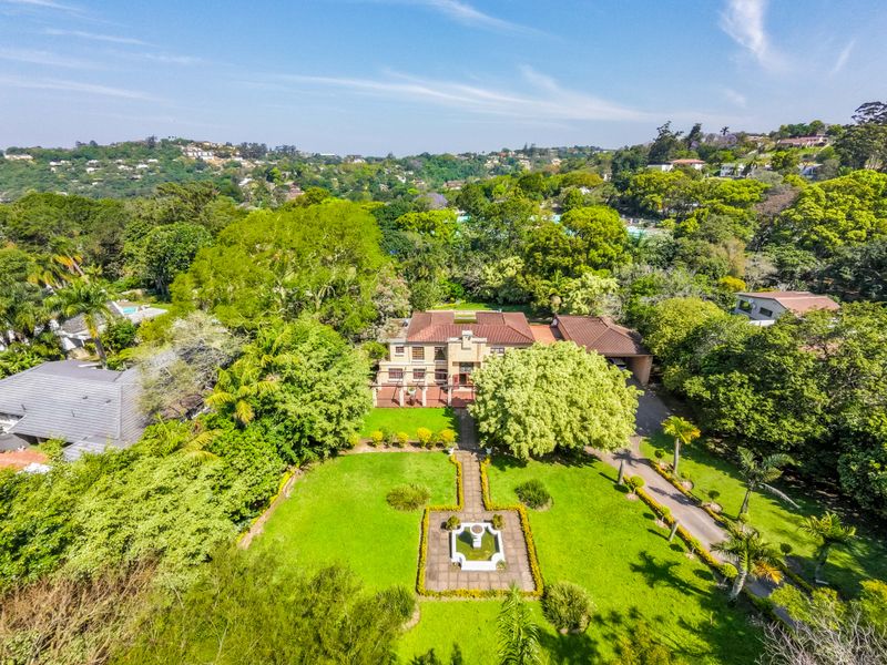 Aerial view of a large residential property featuring a spacious landscaped garden, central water feature, paved driveway, and a substantial multi-level home.