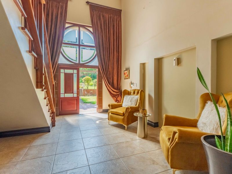 Spacious entrance hall featuring high ceilings, a grand wooden staircase, tiled flooring, and a large arched window providing natural light and garden access.