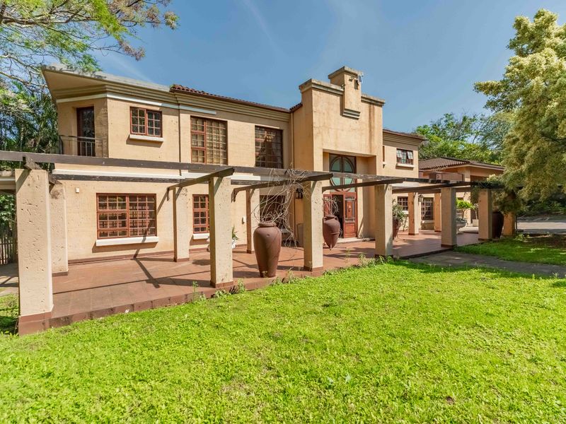 Rear view of a two-story residence featuring a large tiled patio with a pergola, timber-framed windows, and a balcony overlooking the garden.