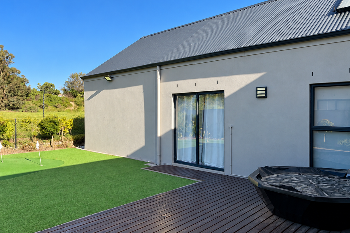 Rear exterior view featuring a modern home with a corrugated metal roof, timber decking, artificial lawn, and integrated exterior lighting.