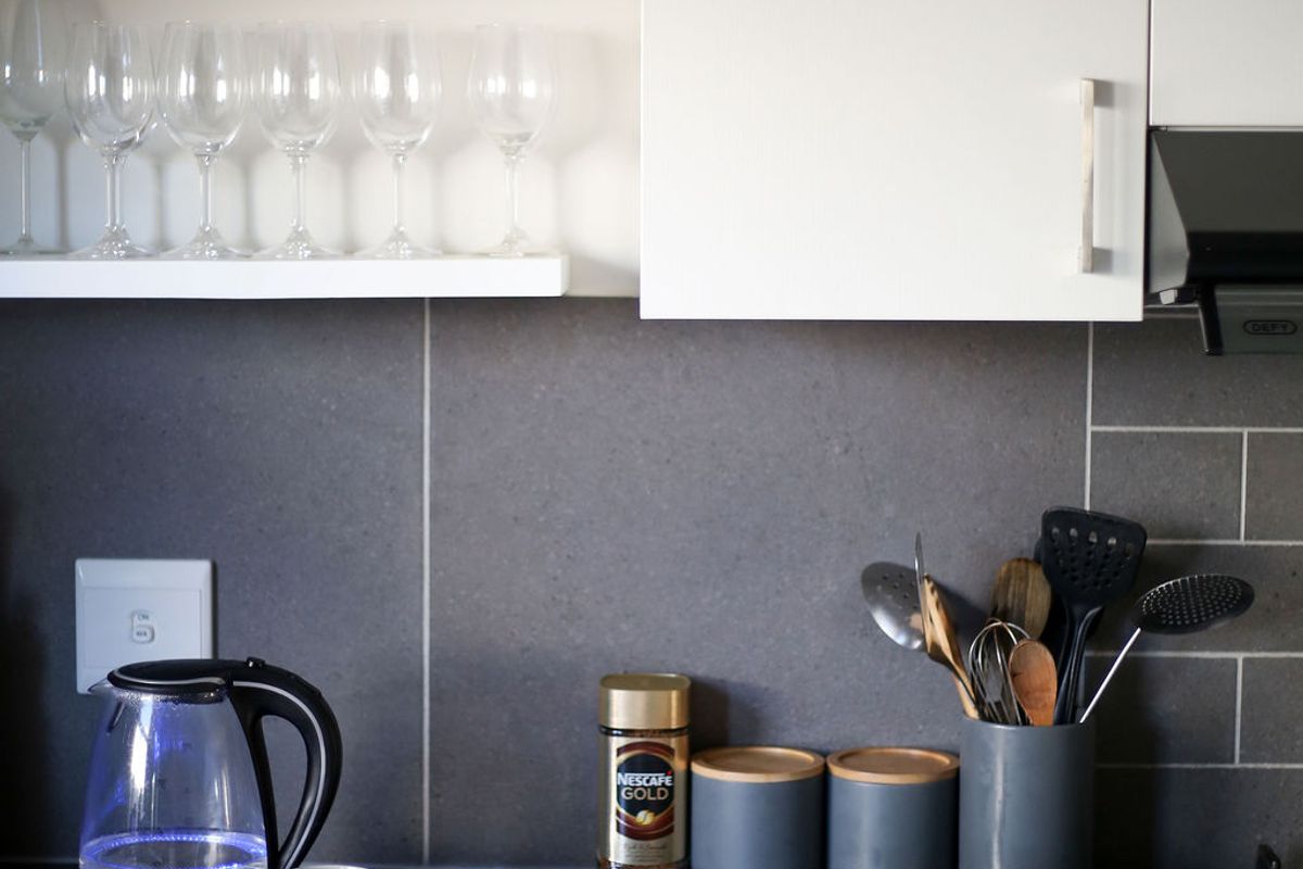 A modern kitchen featuring sleek white cabinetry, dark stone countertops, and a contemporary tiled backsplash with integrated extractor fan and gas hob.