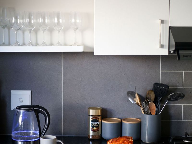 A modern kitchen featuring sleek white cabinetry, dark stone countertops, and a contemporary tiled backsplash with integrated extractor fan and gas hob.