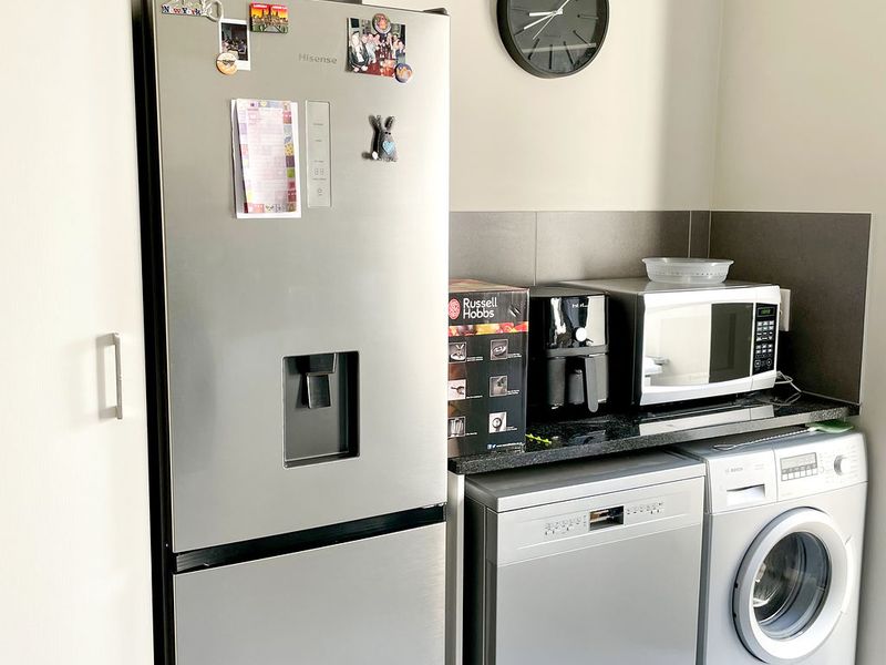 A functional laundry area featuring tiled flooring, granite countertops, and a tiled splashback, providing space for essential appliances and utility storage.