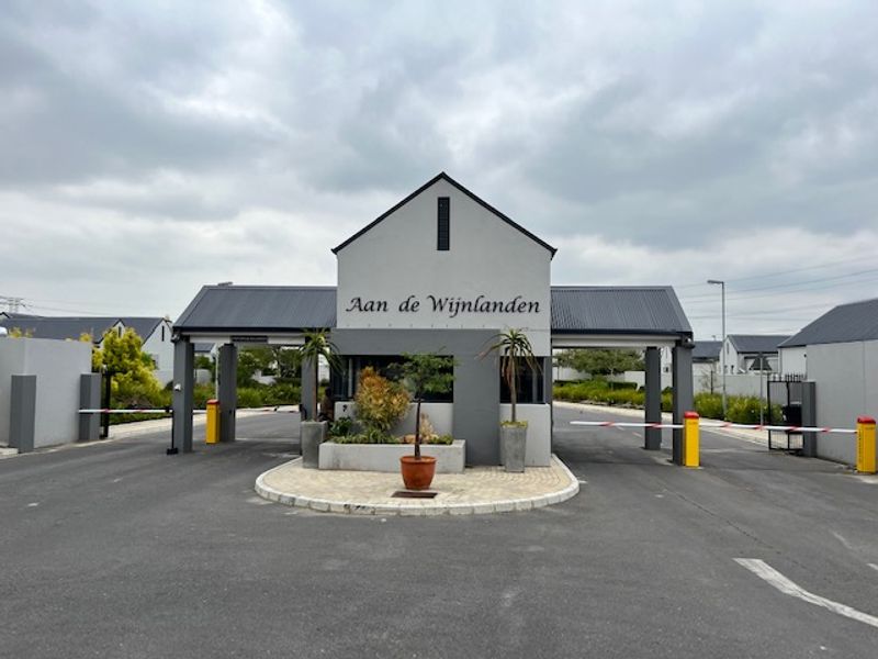 The secure entrance gatehouse of the Aan de Wijnlanden estate, featuring modern architecture, boom gate access control, and paved driveway infrastructure.