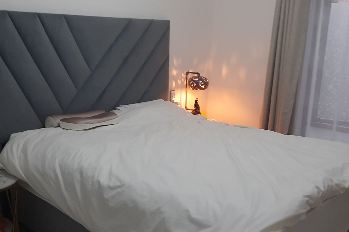 A cozy bedroom featuring a modern upholstered headboard and neutral window treatments, providing a comfortable and well-maintained sleeping space.