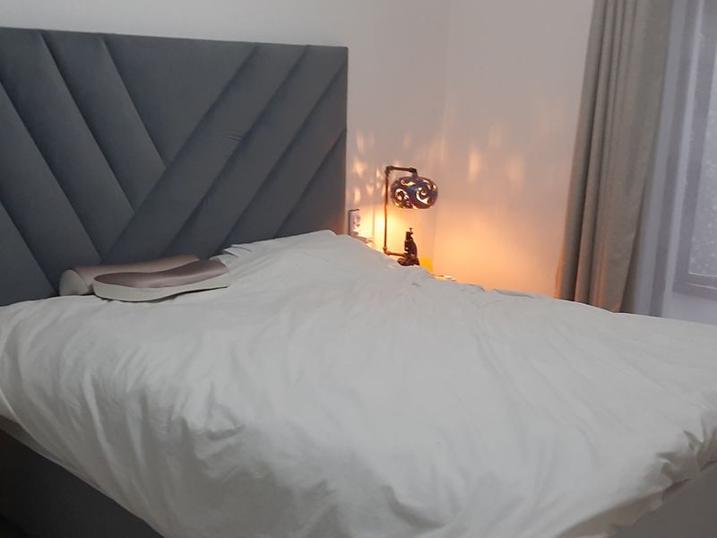 A cozy bedroom featuring a modern upholstered headboard and neutral window treatments, providing a comfortable and well-maintained sleeping space.
