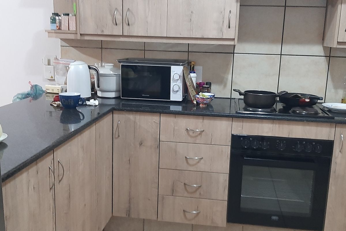 A functional kitchen featuring light wood-look laminate cabinetry, dark granite countertops, a built-in oven, and an electric hob with a tiled backsplash.