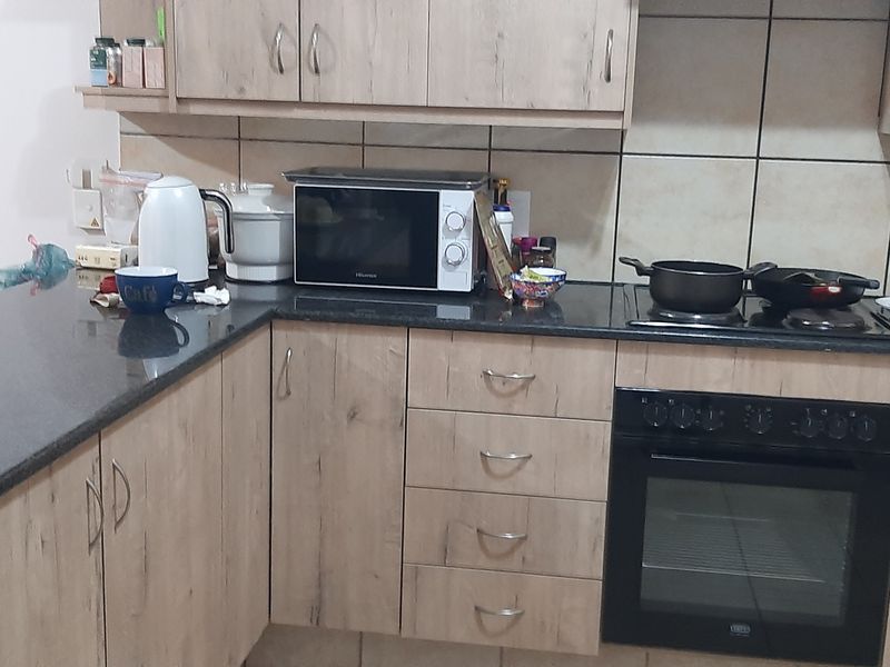 A functional kitchen featuring light wood-look laminate cabinetry, dark granite countertops, a built-in oven, and an electric hob with a tiled backsplash.