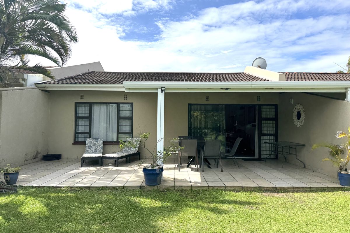 A rear view of the townhouse featuring a paved patio area, sliding glass doors, and a private garden space.