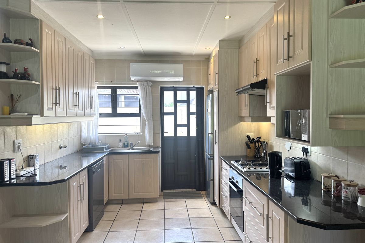 A well-maintained kitchen featuring light wood cabinetry, granite countertops, integrated appliances, and tiled flooring with direct access to the exterior.