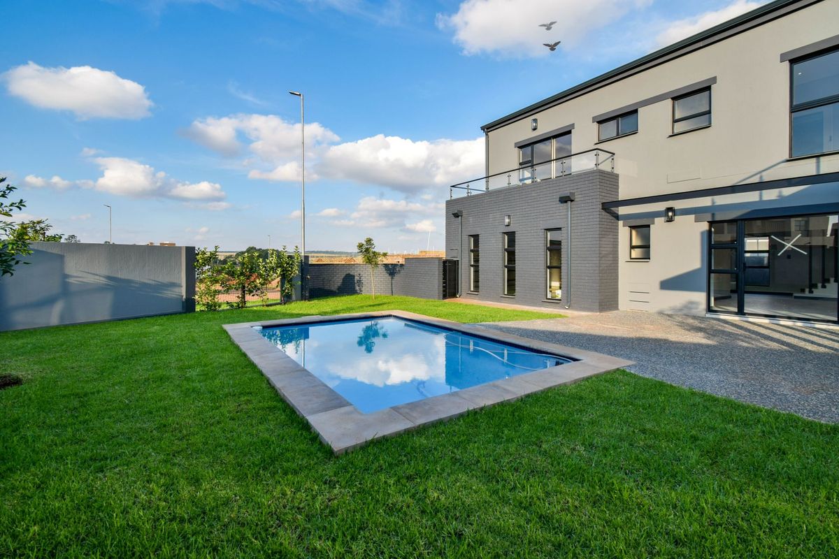A modern rear exterior view featuring a well-maintained lawn, a swimming pool with stone coping, and a contemporary two-story house with a balcony.