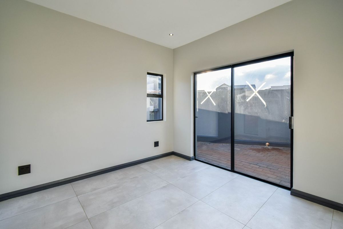 A bright, empty room featuring modern large-format floor tiles, dark-framed sliding glass doors leading to a patio, and recessed ceiling lighting.