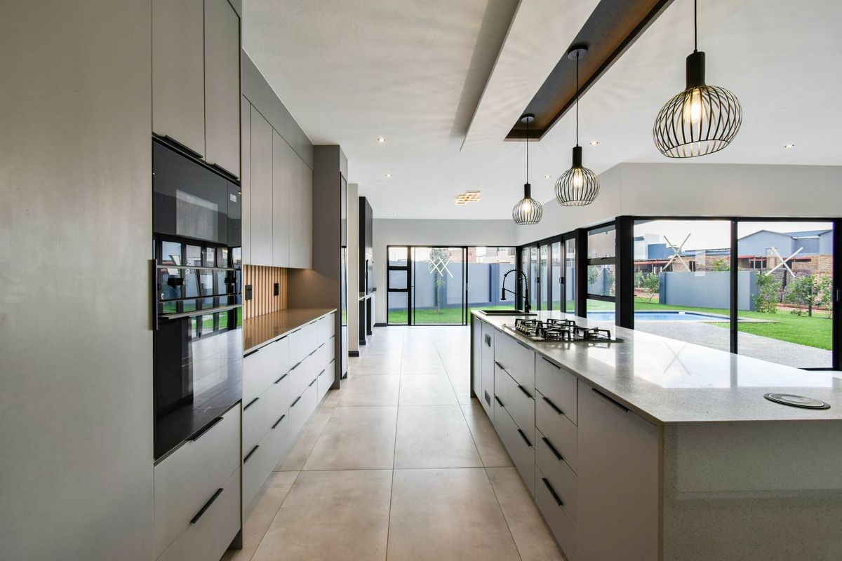 Modern open-plan kitchen featuring sleek grey cabinetry, a large central island with a gas hob, stone countertops, and direct access to the outdoor pool area.