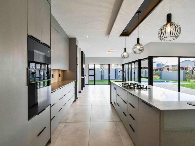 Modern open-plan kitchen featuring sleek grey cabinetry, a large central island with a gas hob, stone countertops, and direct access to the outdoor pool area.