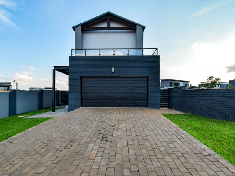 Modern double-story home exterior featuring a dark brick facade, paved driveway, integrated garage, and a glass-railed balcony.