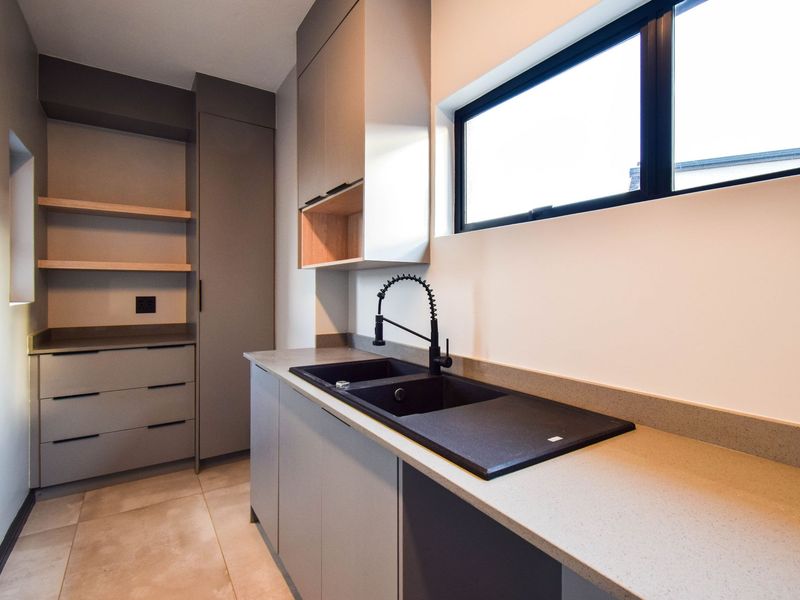 Modern scullery featuring sleek grey cabinetry, stone countertops, a double basin sink with a black gooseneck tap, and open timber shelving.