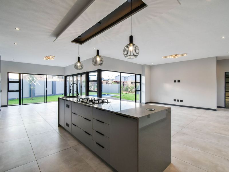 Modern open-plan kitchen and living area featuring a large central island with built-in gas hob, sleek cabinetry, and expansive glass sliding doors to the garden.