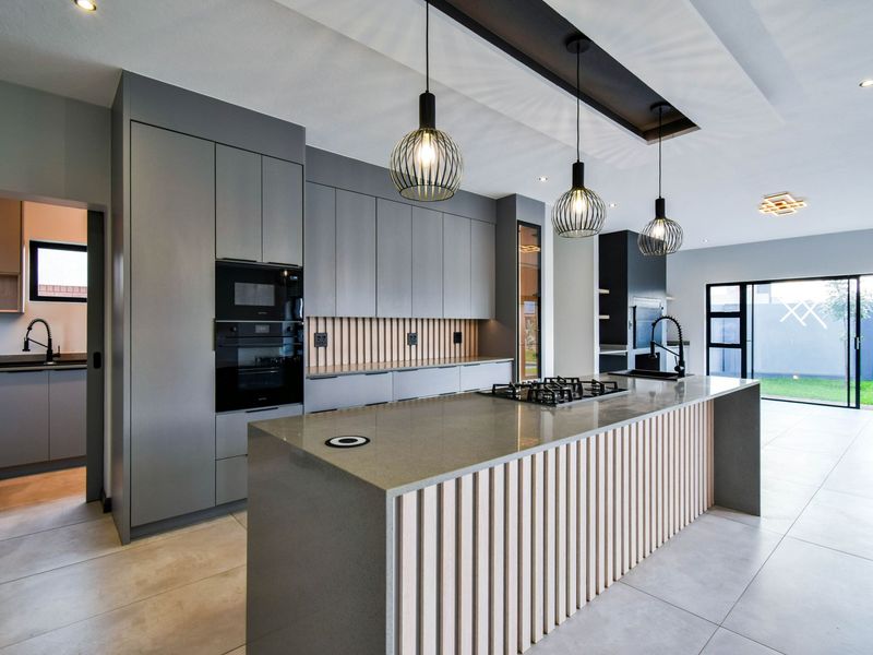 Modern open-plan kitchen featuring a large central island with gas hob, sleek grey cabinetry, integrated appliances, and timber slat detailing.