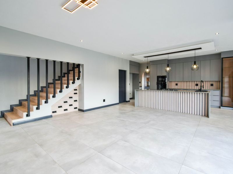 Modern open-plan living area featuring a sleek kitchen with integrated cabinetry, a central island, and a contemporary staircase with timber treads and metal balustrades.