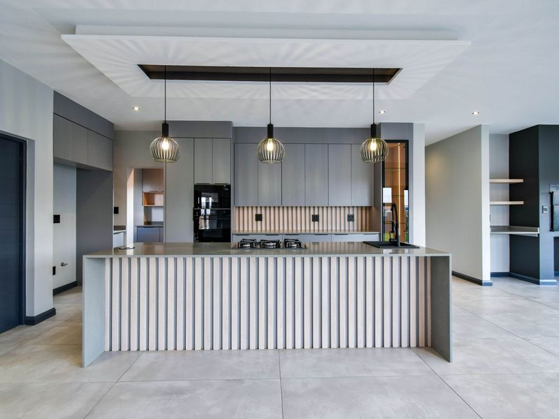 Modern open-plan kitchen featuring a large central island with integrated gas hob, sleek grey cabinetry, and a recessed ceiling detail with pendant lighting.