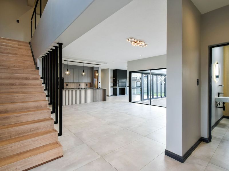 Spacious open-plan living area featuring modern kitchen cabinetry, timber staircase, large sliding doors to the patio, and a contemporary guest bathroom.