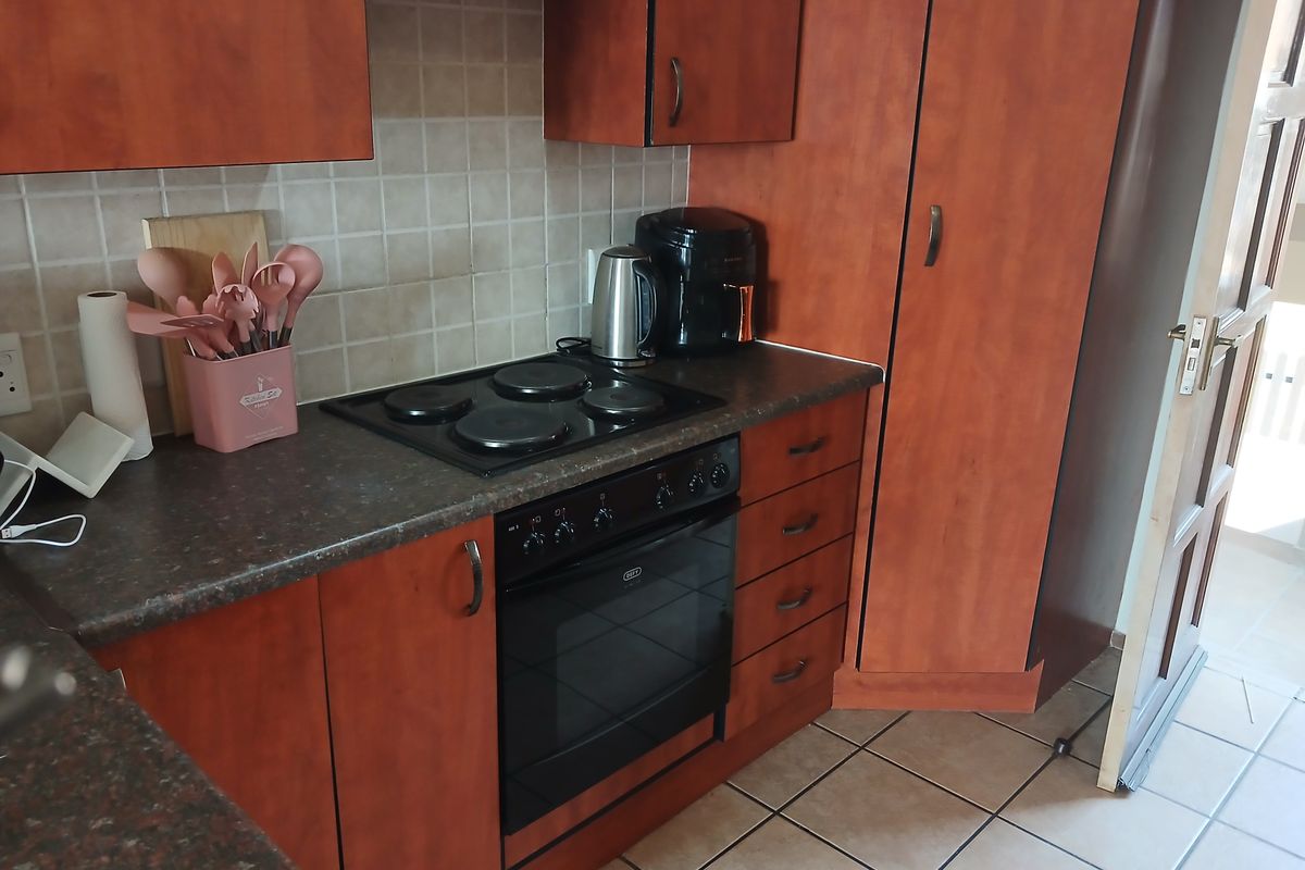 A functional kitchen featuring wood-look laminate cabinetry, a built-in electric oven and hob, tiled backsplash, and durable ceramic floor tiles.