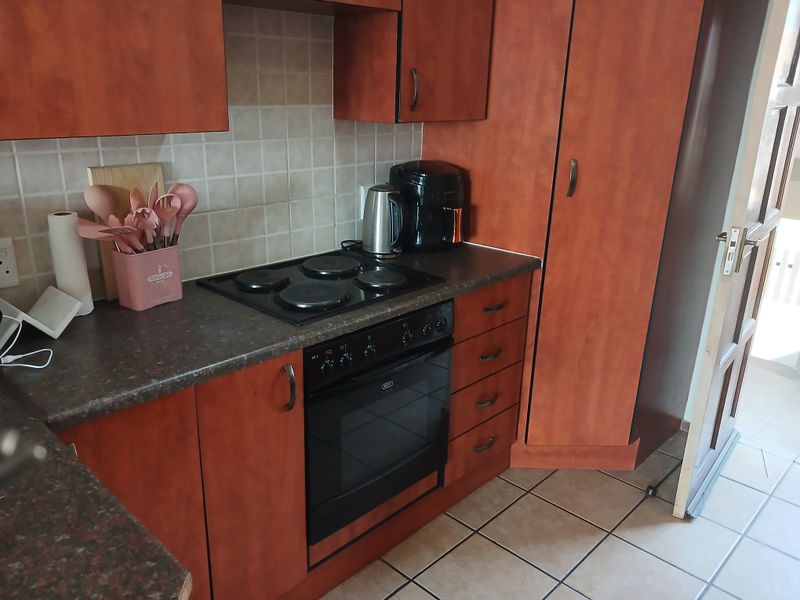 A functional kitchen featuring wood-look laminate cabinetry, a built-in electric oven and hob, tiled backsplash, and durable ceramic floor tiles.