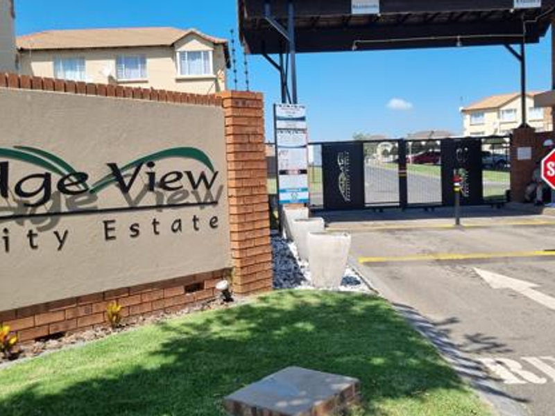 Entrance view of Ridge View Security Estate featuring a brick boundary wall, security gate access, and paved driveway.