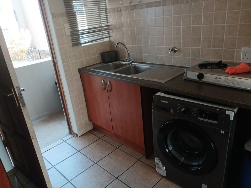A functional laundry area featuring tiled flooring, a double sink with tiled backsplash, built-in cabinetry, and direct access to an outdoor balcony.