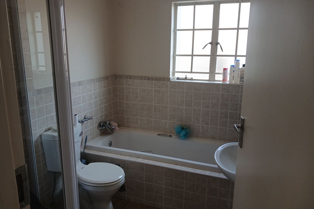 A functional bathroom featuring a built-in bathtub, pedestal basin, toilet, and shower enclosure with tiled splashbacks and a window.