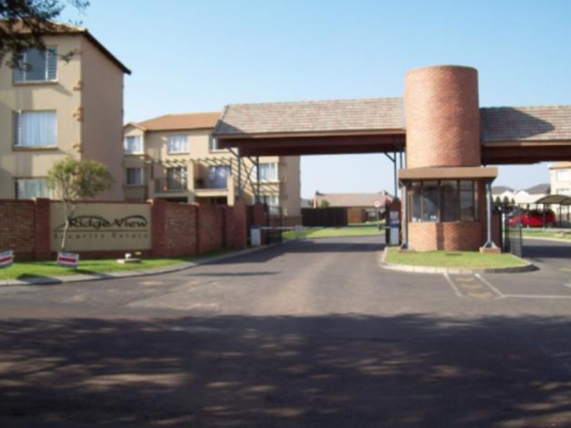 The entrance to RidgeView Security Estate featuring a brick guard house, security boom, and paved access road.