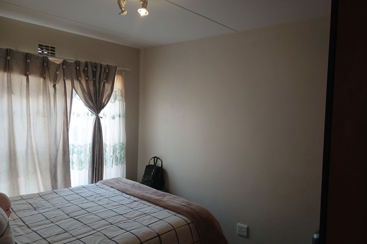 A bedroom featuring neutral walls, a ceiling-mounted spotlight fixture, and a window dressed with curtains.