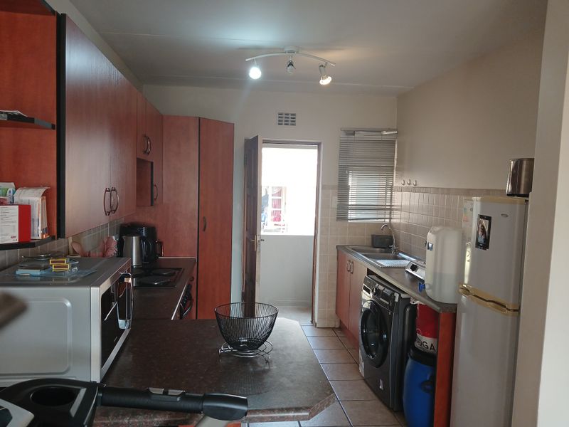 A functional kitchen featuring wood-finish cabinetry, laminate countertops, tiled backsplash, and integrated laundry plumbing, with direct access to an exterior area.
