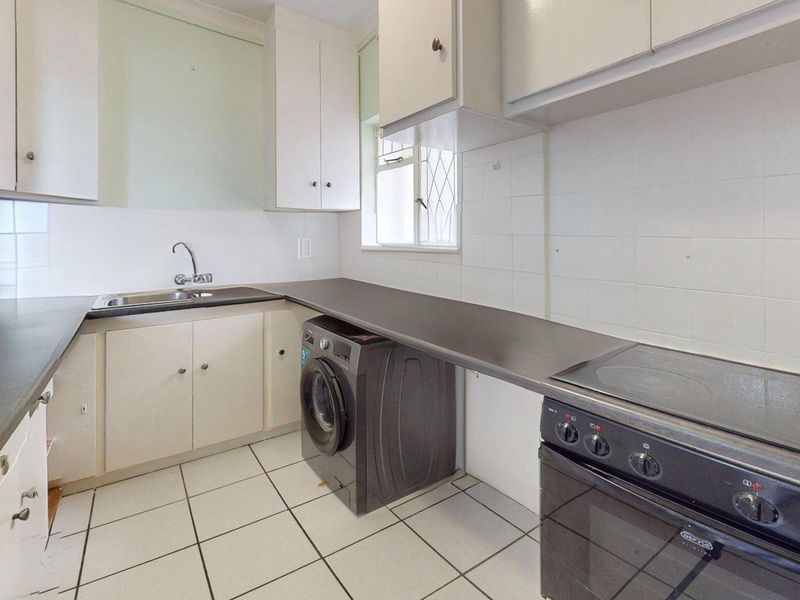 A functional kitchen featuring built-in cabinetry, laminate countertops, a stainless steel sink, and an electric stove with tiled flooring and walls.