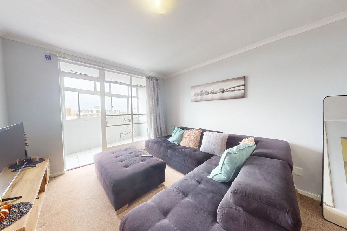 A comfortable living room featuring carpeted flooring, coving, and a large sliding glass door providing access to an attached balcony.