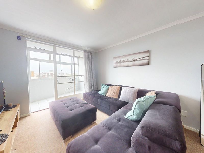A comfortable living room featuring carpeted flooring, coving, and a large sliding glass door providing access to an attached balcony.