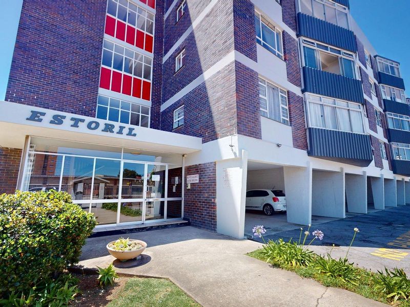 Front exterior view of the Estoril apartment building, featuring a brick facade, glass entrance, and covered parking bays.