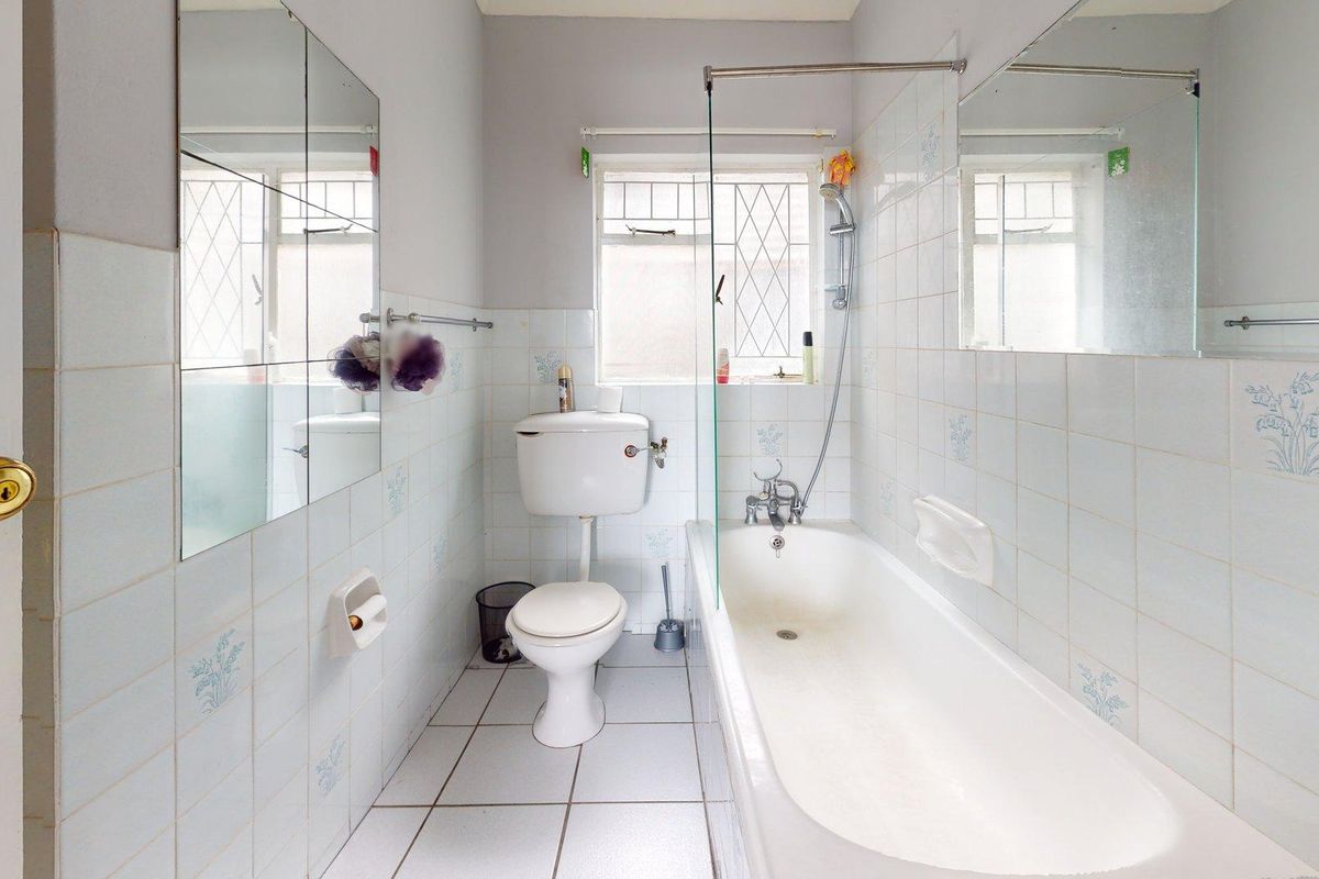 A functional bathroom featuring a bathtub with a glass shower screen, toilet, and tiled finishes, offering a clean and practical layout.