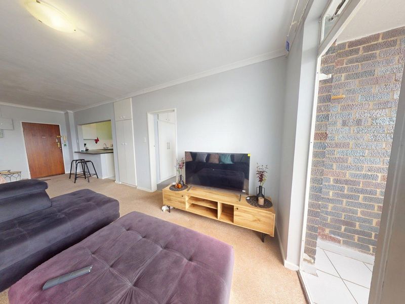 Open plan living area featuring carpeted flooring, built-in storage, and direct access to an enclosed balcony with exposed brickwork.