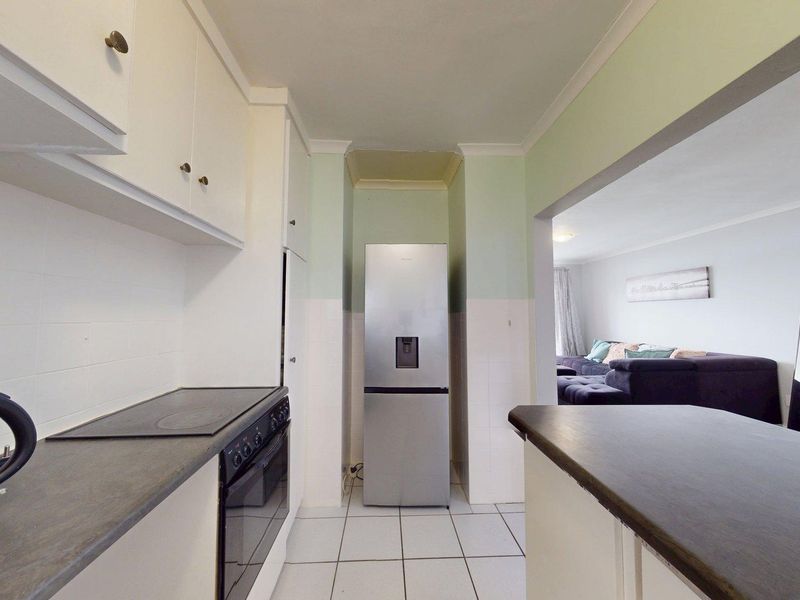 A functional kitchen featuring built-in cabinetry, electric hob, oven, and tiled flooring, with an open-plan layout connecting to the adjacent living area.