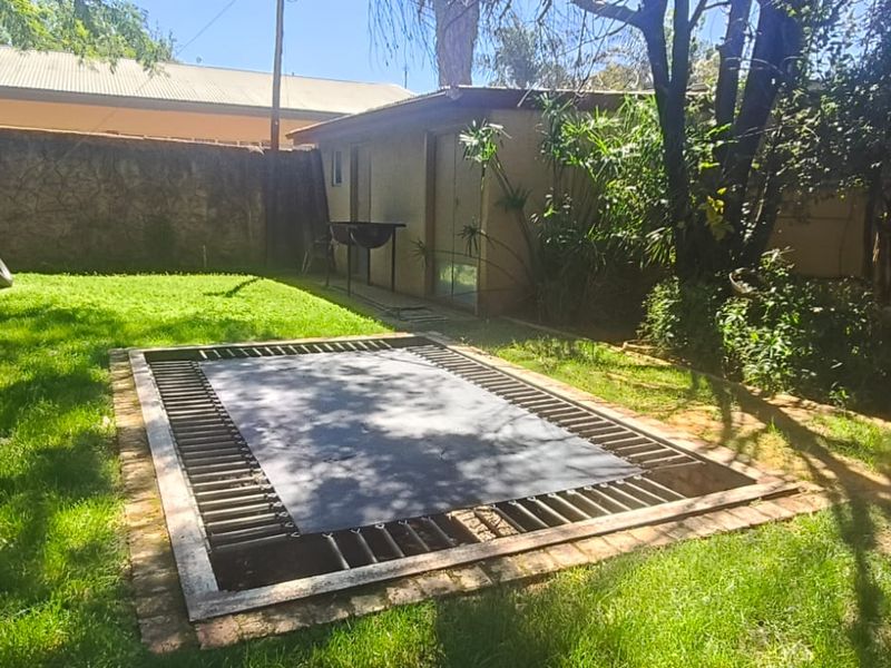 A spacious backyard garden featuring a sunken in-ground trampoline, established lawn, perimeter walling, and a detached outbuilding.