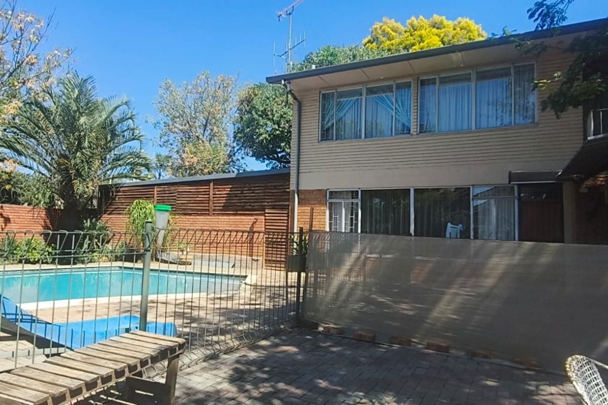 Rear exterior view of the property featuring a swimming pool, paved patio area, and two-story building facade with sliding glass doors.