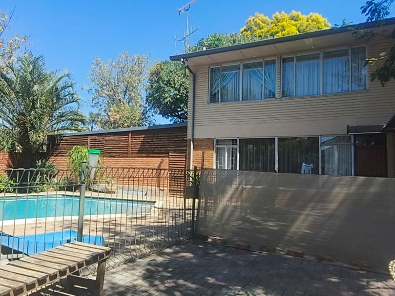 Rear exterior view of the property featuring a swimming pool, paved patio area, and two-story building facade with sliding glass doors.