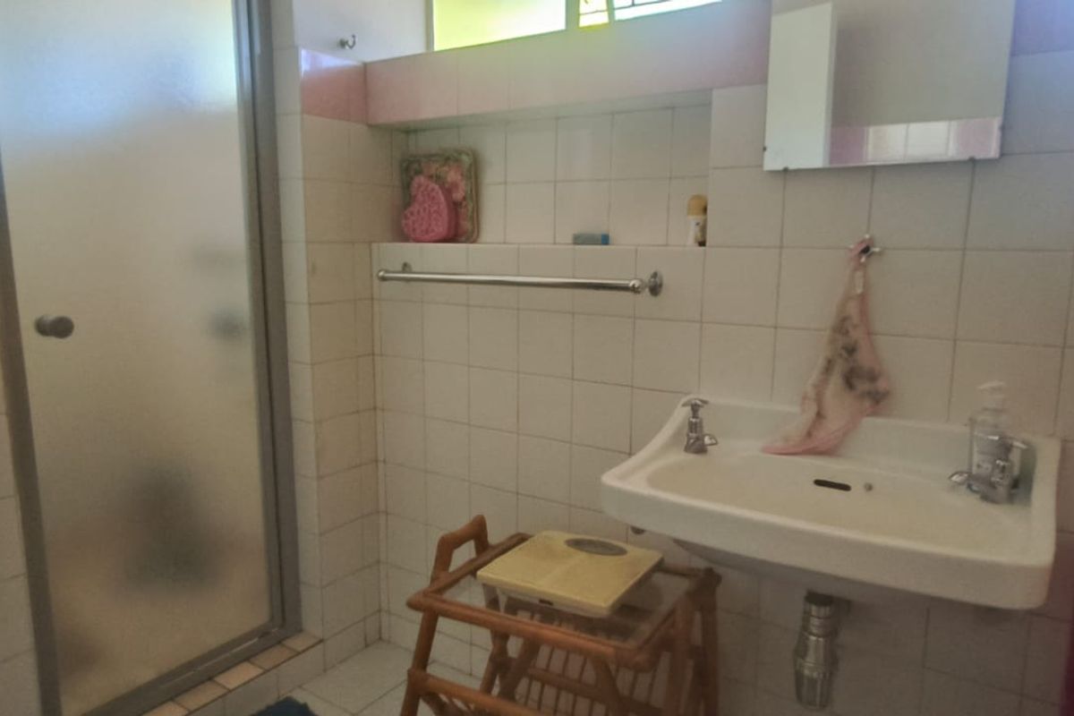 A functional bathroom featuring a wall-mounted basin, shower enclosure, and tiled walls with integrated shelving, offering potential for a modern renovation.