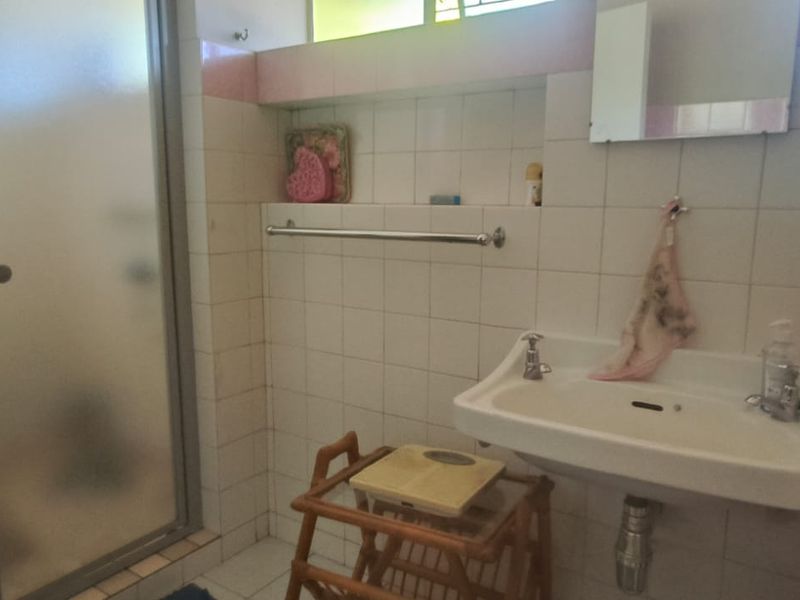 A functional bathroom featuring a wall-mounted basin, shower enclosure, and tiled walls with integrated shelving, offering potential for a modern renovation.