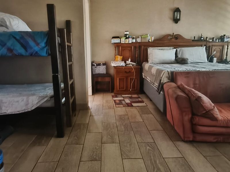 A spacious bedroom featuring tiled flooring and a wall-mounted light fixture, currently configured with multiple sleeping areas.